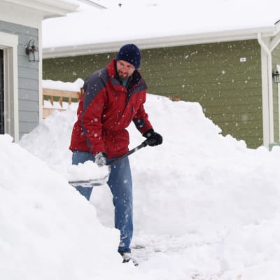 En man skyfflar snö utanför en villa.