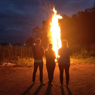 Kristine Andora Nilsen, Elisabeth Gjestland och Jontti Granbacka betraktar midsommarbrasan på Fölisön