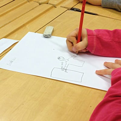 Flicka ritar på ett papper vid en pulpet