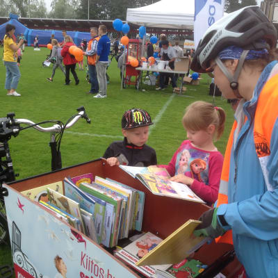 Lapset katsovat polkupyörästä tehdyn Kuopion kaupunginkirjaston kirjastopyörän kirjoja Kuopion Väinölänniemellä.  