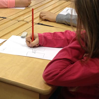 Flicka ritar på ett papper vid en pulpet