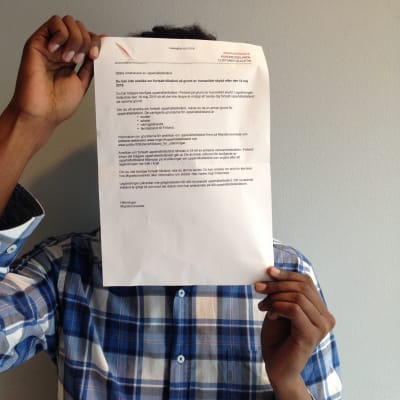En somalisk man håller upp Migrationsverkets brev framför sitt ansikte.