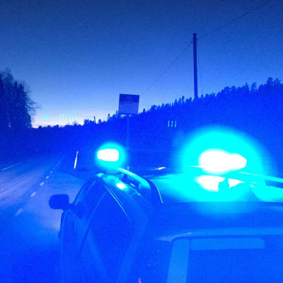 Bil med blåljus kör i mörker på landsväg.