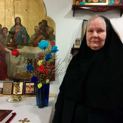 Mustaan nunnanviittaan pukeutunut nunna Elisabet seisoo Mikonkadulla sijaitsevan pienen ortodoksikappelin alttarin edessä. Taustalla ikoneita ja itäiseentyyliin tehtyjä virpomisvitsoja, joissa on silkkipaperista tehtyjä eri värisiä kukkia. Pöydällä on myös raamattu ja koristeellinen kynttilänjalka.