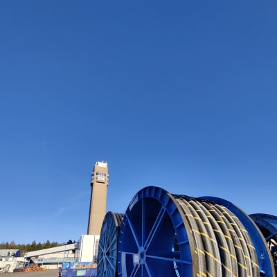 En rulle med kabel som ska sättas ut på havsbotten. I bakgrunden syns ett torn på ett fabriksområde där det tillverkas kablar.