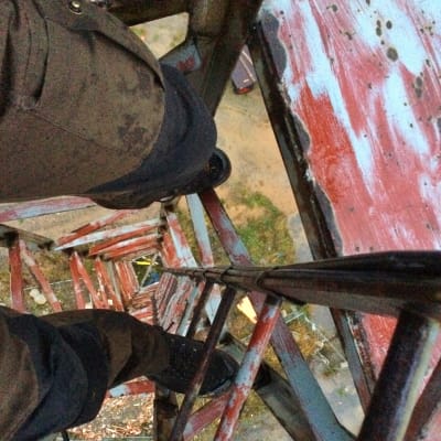 Bild av benen av en man som klättrat högt upp i ett torn och tittar neråt.