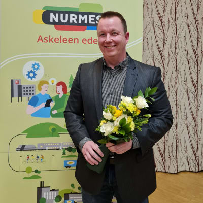 Nurmeksen uusi kaupunginjohtaja Pasi Parkkinen hymyilee lähikuvassa kukkakimppu kädessä valituksi tulemisen jälkeen. 