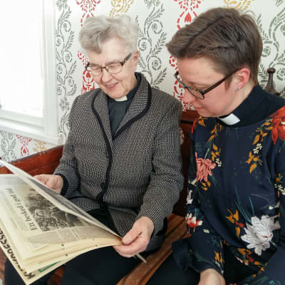 Ulla Östman och Malin Lindblom tittar på tidningsklipp från 1988 då de första kvinnorna prästvigdes.