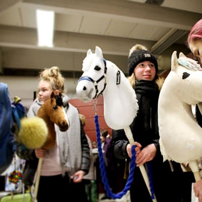 Tytöt ja keppihevoset jonottavat laivaterminaalissa.