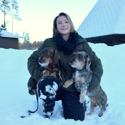 Nainen poseeraa ulkona kahden mäyräkoiran kanssa.