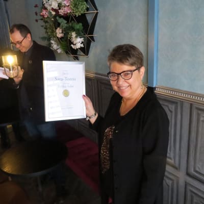 Nainen hymyilee kunniakirja kädessään.