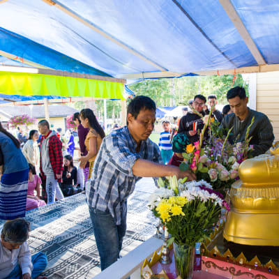 Ihmiset tuovat kukkia buddhan patsaalle.