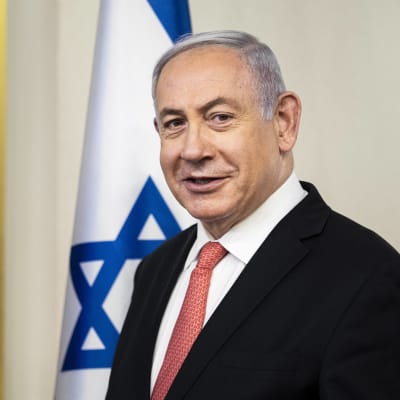 Pääministeri Benjamin Netanjahu katsoo kameraan seisten Israelin lipun edessä.