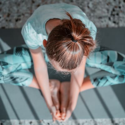 En kvinna i träningskläder sitter på en yogamatta och tänjer.