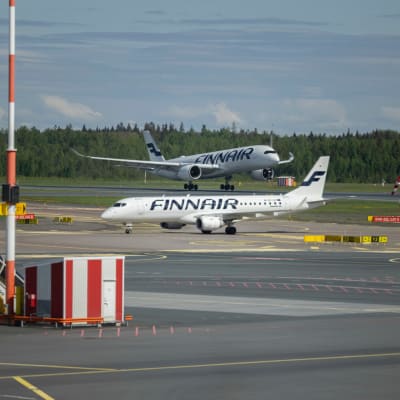 Kaksi Finnairin sinivalkoista konetta Helsinki-Vantaan lentokentällä, etualalla lentokenttäkalustoa.