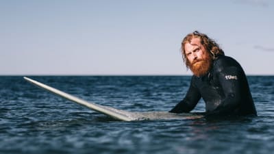 Kristofer Hivju som Erik står till midjan i vattnet med surbräda. Inga vågor.