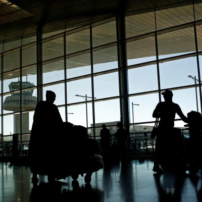Passagerare i en flygterminal, i bakgrunden lyktstolpar och ett flygledningstorn.