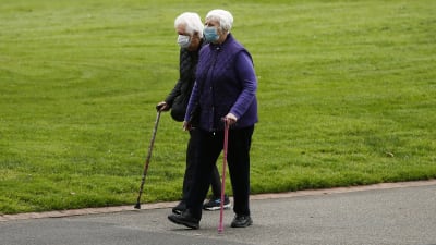 Två äldre personer promenerar utomhus i Victoria, Australien. De bär munskydd.