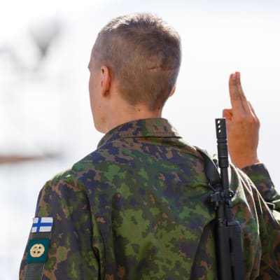 Två soldater med Finlands flagga på armen på uniformen står med ryggen mot kameran.