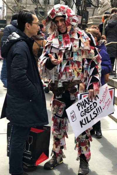 Man iklädd dräkt dekorerad med tygstycken som föreställer sedlar, protest mot dyr medicin i USA