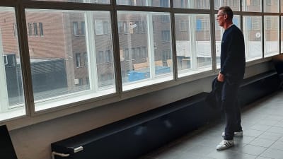 Medelålders man står och tittar ut genom ett stort fönster.