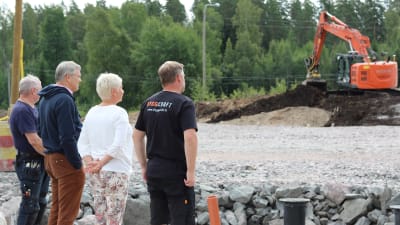 Fyra personer står på ett område och tittar på en gräsmaskin som arbetar.
