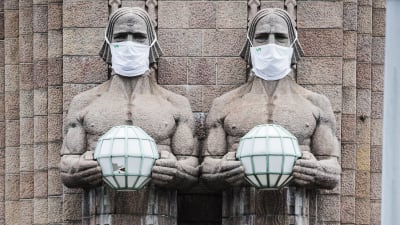 I bild syns en skulptur "Lyktbärare" utanför Helsingfors tågstation som bär munskydd.
