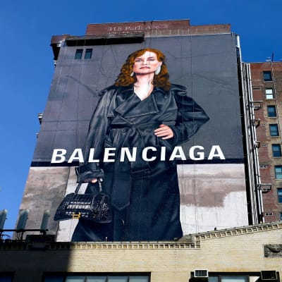 Isabelle Huppert pitkässsä takissa Balenciagakan mainoksessa joka on kiinnitetty talon seinään. Kuva on valtava.