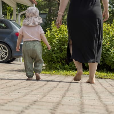 Äiti ja lapsi kävelevät paljain jaloin pihamaalla