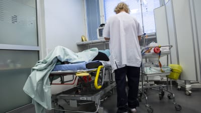 En sjukskötare sätter dropp i en patient som ligger i en säng.