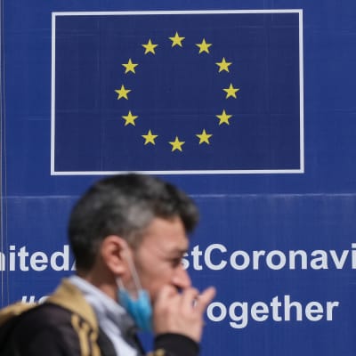 Mies kävelee EU-julisteen ohi, jossa kerrotaan yhteistyöstä koronakriisissä.