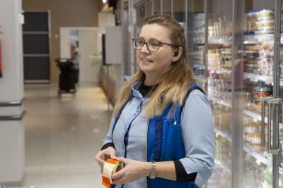 En kvinna i s-gruppens blå dräkt står i en butik och håller i en rulle med orange rea-lappar.