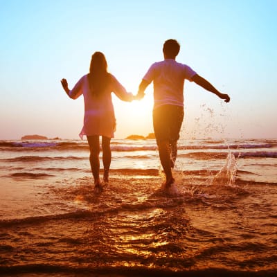 Man och kvinna håller varandra i handen på en strand i solnedgången. 