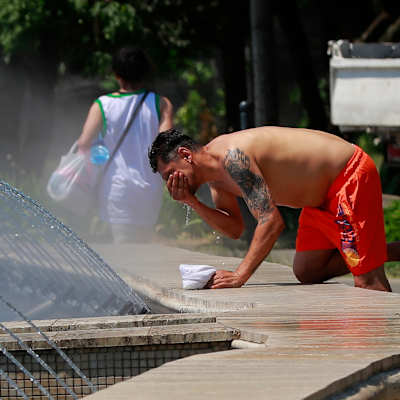 En man i röda shorts svalkar sig med vatten från en fontän.
