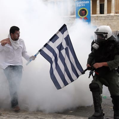 Grekisk man som håller flagga framför kravallpoliser