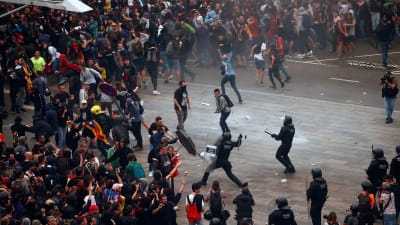 Demonstrationer vid den internationella flygplatsen El Prat i Barcelona. I bildens mitt syns en kravallpolis som motar ett slag mot en demonstrant. 