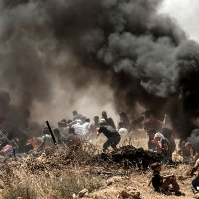 Palestinier i närheten av gränsstängslet mellan Gazaremsan och Israel bland rökbomber, barn i förgrunden. 