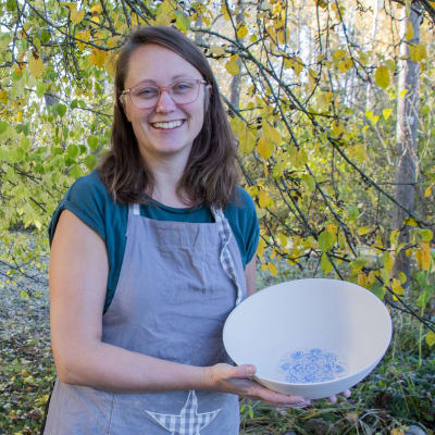 Linda Öhman står under ett äppelträd som håller på att tappa sina blad. I sina händer har hon en keramikskål som hon själv har tillverkat.