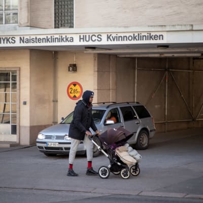 En kvinna med barnvagn utanför en byggnad. På bilden Kvinnokliniken i Helsingfors