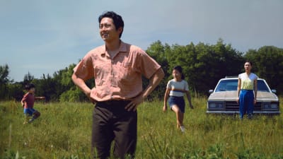 Jacob (Steven Yeun) och hans fru Monica (Yeri Han) och barnen David och Anne står på ett grönt fält, Jacob ser glad och nöjd ut.