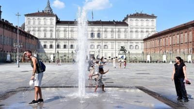 Turister svalkar sig i fontänen på ett torg i Torino i Italien