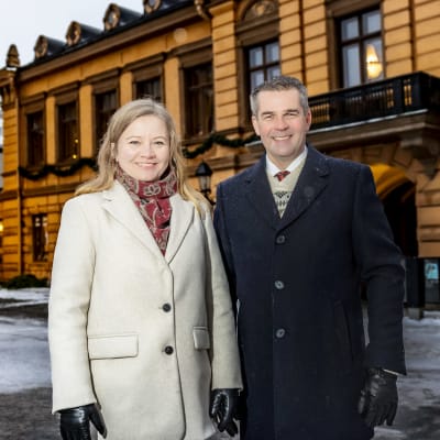 En kvinna och en man står framför Brinkalahuset, i bakgrunden lyser en julgran.