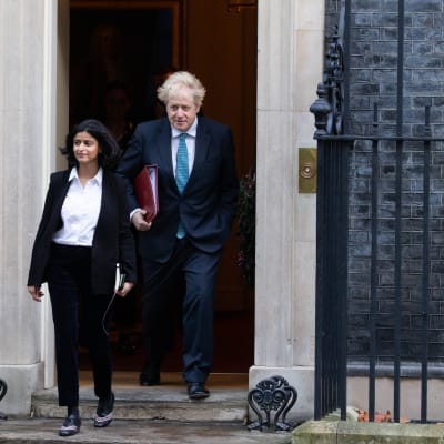 Munira Mirza (kavaj och skjorta) går ner för trappor framför Boris Johnson (kostym med slips).