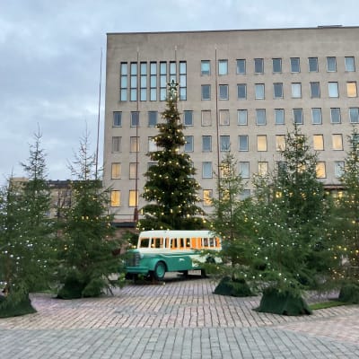 Leikkibussi valaistujen kuusien keskellä Kotkan Kauppatorilla. Taustalla on kaupungintalo.