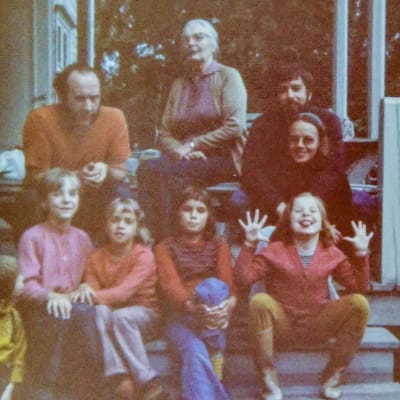 Vuxna och barn sitter på en trappa. Flickan längst till höger visar tungan och spretar med fingrarna.