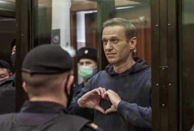 Aleksej Navalnyj står i en glasbur omgiven av poliser och formar ett hjärta med händerna.   