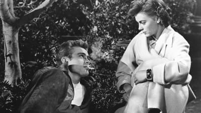 James dean ligger och röker, Natalie Wood ser på honom i vit kappa