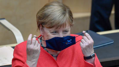 Angela Merkel sätter på sig ett munskydd med tysk EU-logo. 