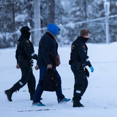 Personer från Gränsmyndigheten går med en asylsökande i vinterväder.