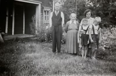 Kauko Purasen perhettä isovanhempien kotipihalla, seisovat ryhmässä ja katsovat kameraan.